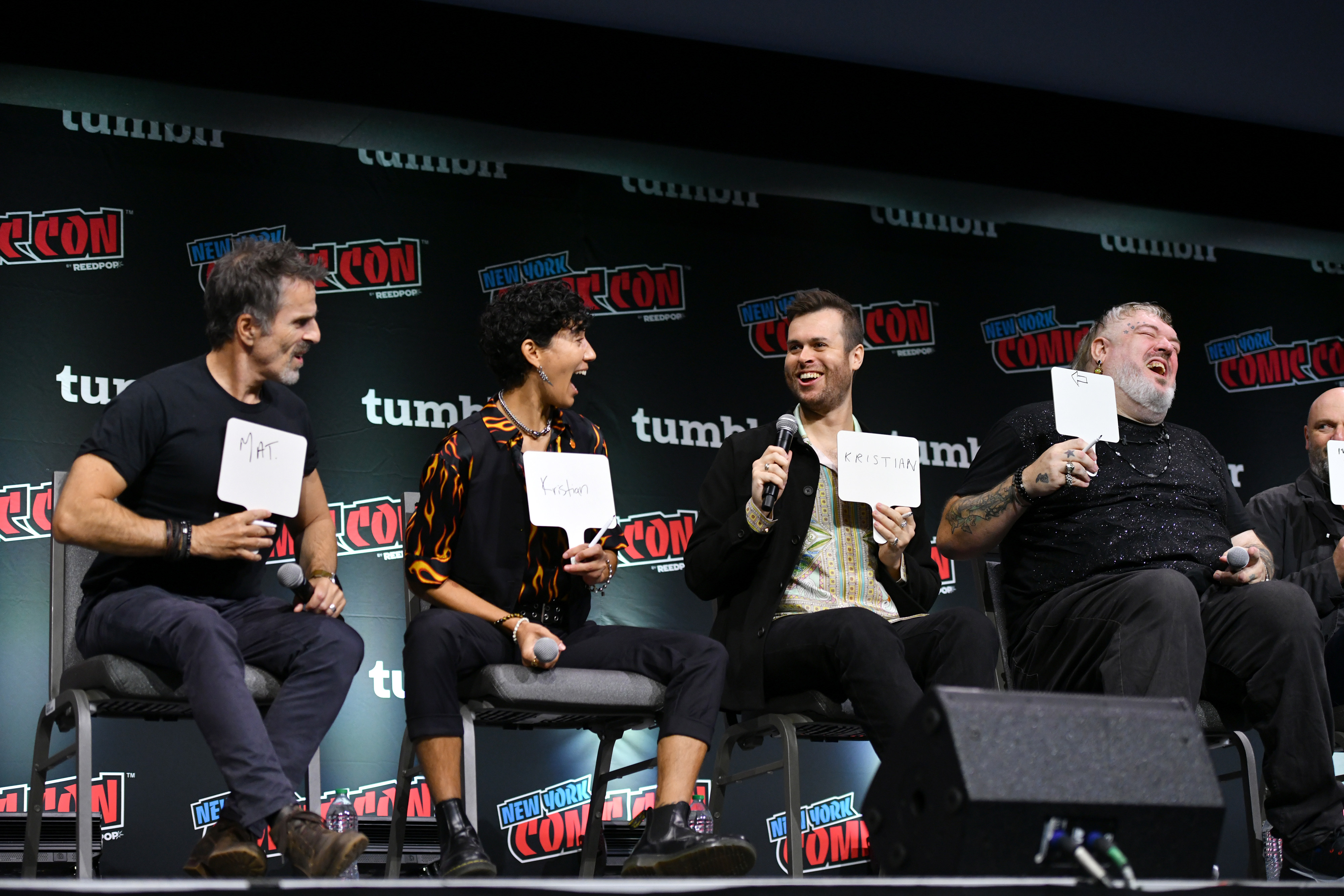 Con O’Neill, Vico Ortiz, Nathan Foad and Kristian Nairn sit on the NYCC 2023 stage with whiteboards playing a Newlywed Game-style game